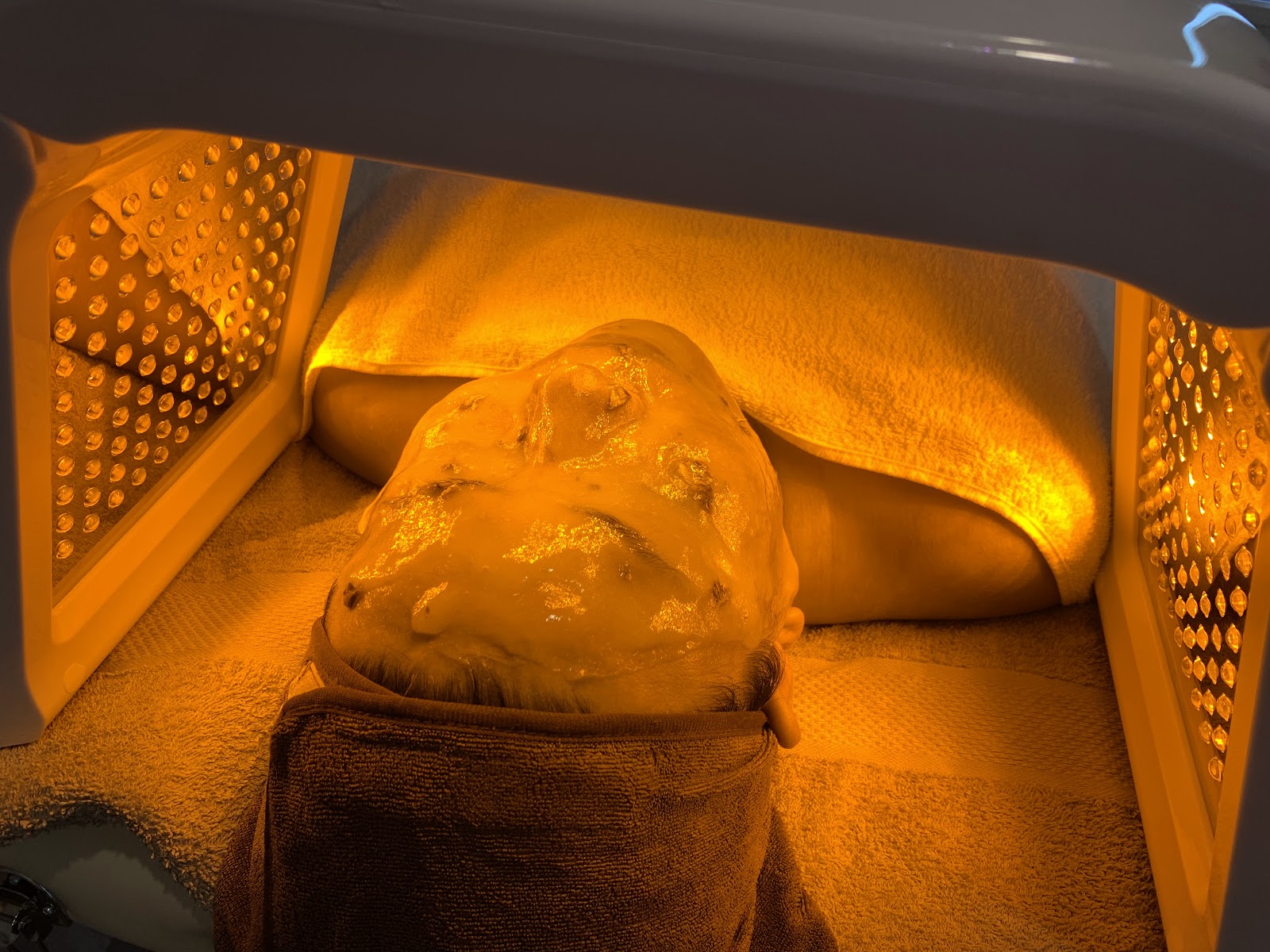 A client lying under a warm LED light panel during a facial