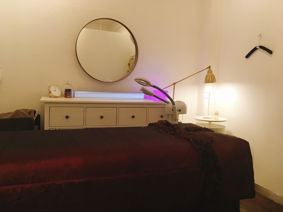 The treatment room at K Beauty Skin Clinics, with a round brass mirror, magnifier lamp and treatment bed